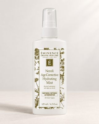 A white plastic spray bottle of Eminence Organic Skin Care Neroli Age Corrective Hydrating Mist, featuring a white cap and a detailed botanical label with green illustrations.